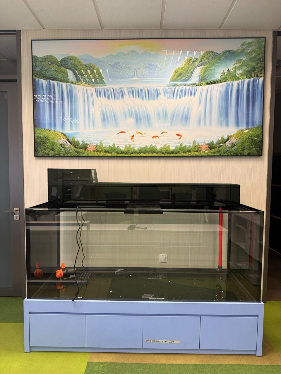 A cabinet tank installed beneath a waterfall mural.